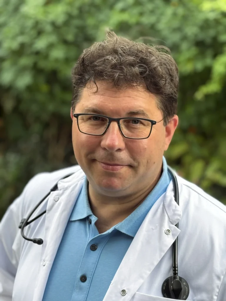 Dr. Michael Grundbichler stehend vor grünem Hintergrund in Salzburg.